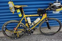 Full left-side view of yellow road bike showing frame, wheels, water bottles and aero bars