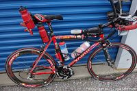 Full side profile of red Aquila bicycle showing frame, wheels, aero bars and accessories.