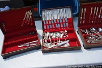 Three wooden presentation cases of plated flatware displayed on a white table surface; red velvet-lined interiors with knives, forks, spoons visibly arranged in compartments and loosely placed in cases.