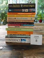 Stack of paperback books featuring mainly science fiction and fantasy titles including Good Omens, The Postman, The Midwich Cuckoos, The Eye of the Heron, Gulliver's Travels, One Flew Over the Cuckoo's Nest, Max and the Cats, Surfacing, Moral Disorder, The Virgin and the Gypsy, Interface