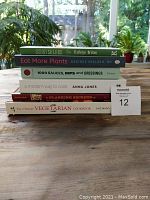 Stacked view of six cookbooks with titles visible, arranged on a table with plants in the background.