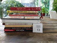 Stack of 12 books on a wooden table with visible titles and auction lot number