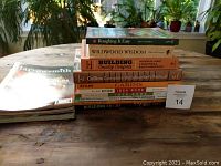 Stack of woodworking and renovation books on a wooden table, showing titles like Roughing It Easy, Wildwood Wisdom, Building Country Controls, and Collins Complete Woodworker's Manual.