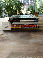 Stack of seven adult graphic novels with spines showing titles and authors, arranged on wooden table with natural light.