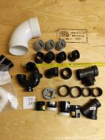 Various new black and white plastic plumbing fittings arranged on plywood.