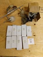 Nine white boxes each containing black steel interior door hinges, with some door hardware items and lighting fixtures on a wood surface.