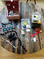 Full layout of sewing notions and crafting supplies on round wooden table, including sewing box, scissors, trims, zip, craft kit, felting boards.