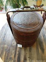 Photo of stacked tiered woven basket from above, showing detailed woven pattern on lid and brass hardware on handle.