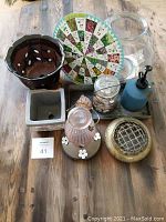 Garden items displayed on a wooden table including pots, flower frog, mister, glass containers, shells, and planting guide wheel.