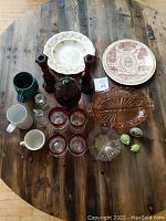 Full overhead view of all items including plates, glasses, candle holders, salt and pepper shakers, mugs, and divided pink glass dish.