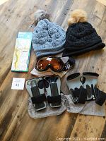 All items in the lot displayed together on a wooden surface including two toques, ski goggles, wrist protectors, and laminated map.