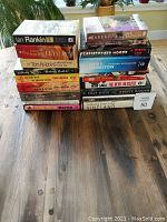 Photo of stacked and spread books on a wooden table, showing varied titles and sizes.
