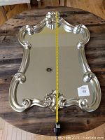 Full view of the rectangular decorative mirror laying on wooden table with measuring tape showing height.
