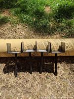 Four black metal post holders with U-shaped bracket and spike standing upright on grass in front of a Quik-Tube cement tube.