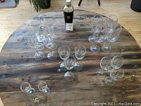 Top-view photo showing multiple glassware items arranged on wooden table, including etched wine glasses and crystal skull cocktail shaker in center back.