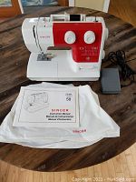 Full view of sewing machine with foot pedal, manual on dust cover, and machine on wooden table.