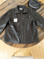 Black leather jacket and black straw hat displayed on a wooden table