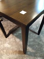 Close-up showing the wood grain brown square table top corner and part of a black leg.