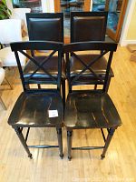 Front view of the pair of black rustic wooden bar stools with cross-back design and worn seats.