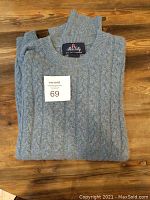 Folded light blue men's cashmere sweater by Allen Solly on wooden surface.