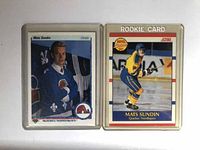 Two Mats Sundin hockey cards in plastic protective cases. One card shows Sundin in a Quebec Nordiques blue jersey posing with arms crossed. The other shows Sundin in action skating wearing Quebec Nordiques yellow and blue jersey. Both have front and back visible in two separate photos.