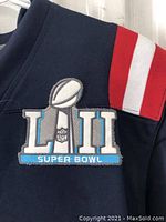 Close-up photo of Super Bowl LII patch with trophy and NFL logo on navy blue jersey fabric with red and white shoulder stripes.