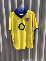 Front view of yellow Arsenal soccer jersey with blue collar, O2 sponsor logo, and club crest.