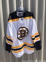 Front view of white Boston Bruins hockey jersey with black and yellow accents and Boston Bruins logo on chest.