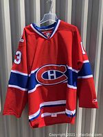 Front view of red Montreal Canadiens hockey jersey with the Canadiens logo and number 13 on sleeves.