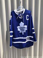 Front view of blue Toronto Maple Leafs hockey jersey with Reebok tag, captain's C, large white maple leaf logo, and lace-up collar.