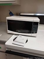 White RCA microwave oven model RMW733 sitting on a kitchen stove with black glass door and digital keypad at right.