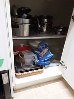 Shelf of stainless steel pots, orange enameled cast iron pots, glass bakeware, colorful oven mitts, and a glass measuring cup.