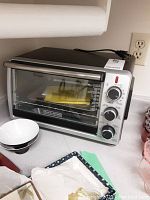 Black & Decker toaster oven showing front view with dials and closed door, power cord visible on top.