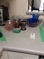 Wide shot showing the 8 cranberry glasses, large pink bowl, Bavarian blue and gold vase, clear molded dish, and blue ribbed vase.