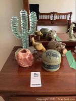 Overview of glass cactus, pottery piggy bank, orca bowl with lid, ceramic birds, and stone candle holder on wooden table