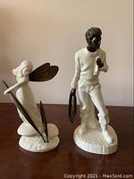 Two Minton porcelain figurines on a flat surface, one fairy figure with brass wings and leaves and one fisherman figure with brass accents.