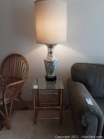 Full view of the lit Japanese style ceramic lamp on top of brass framed glass side table next to sofa and wicker chair.