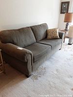 Front side view of green apartment sofa with throw pillow, showing seat cushions and armrest.