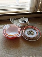 Three nested Pyrex mixing bowls in varying orange and white shades plus set of 4 ceramic pasta bowls and large serving plate with decorative 'Pasta' design.
