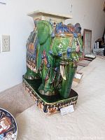 Side view of green ceramic elephant figurine stool showing detailed paint work and saddle blanket design.