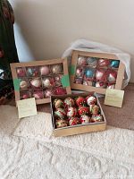 Two boxes of hand painted glass Christmas ornaments labeled as made in Germany with handwritten notes visible, plus one box of fabric decorated balls.