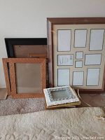Group photo showing various picture frames resting on carpet against wall including multi-photo frame and other wood and metal frames.