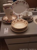 View of large vase with matching base alongside various china plates and bowls with floral patterns.