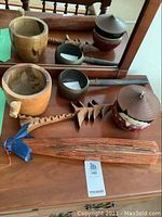 Photo showing the antique Japanese iron bowl with a long handle, lacquered girl bowl with lid, vintage parasol, wooden mortar and pestle, and wooden ladle laid out on a wood surface.