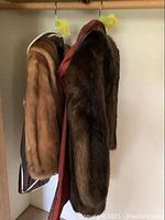 Two fur coats hanging side by side on hangers in a closet, one longer and one shorter coat