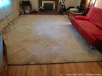 Full view of the large cream and light brown patterned rug laid out in a living room, showing geometric pixelated design and faint stains.