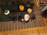 Multiple black metal candle holders with lit and unlit pillar candles arranged in front of fireplace hearth.