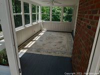 Full view of large wool oriental rug on screened porch floor, showing overall ivory color and border pattern