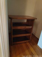 Front view of small wooden shoe holder stand with three shelves on wooden floor.