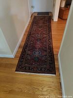 Full view of the red Oriental wool rug runner laid out on hardwood floor in hallway, showing entire length and pattern details.